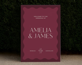 May include: A burgundy wedding welcome sign with a wavy border. The sign reads "WELCOME TO THE WEDDING OF AMELIA & JAMES" in a serif font. Below the names are the date "22 MAR 25" and the location "BRISBANE QUEENSLAND".