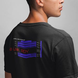 Peut inclure: T-shirt noir avec un motif graphique au dos. Le motif comprend le texte "NEURAL CAGE OVERRIDE" au-dessus de lignes bleues et violettes et le texte "LNK RDY" en rouge.