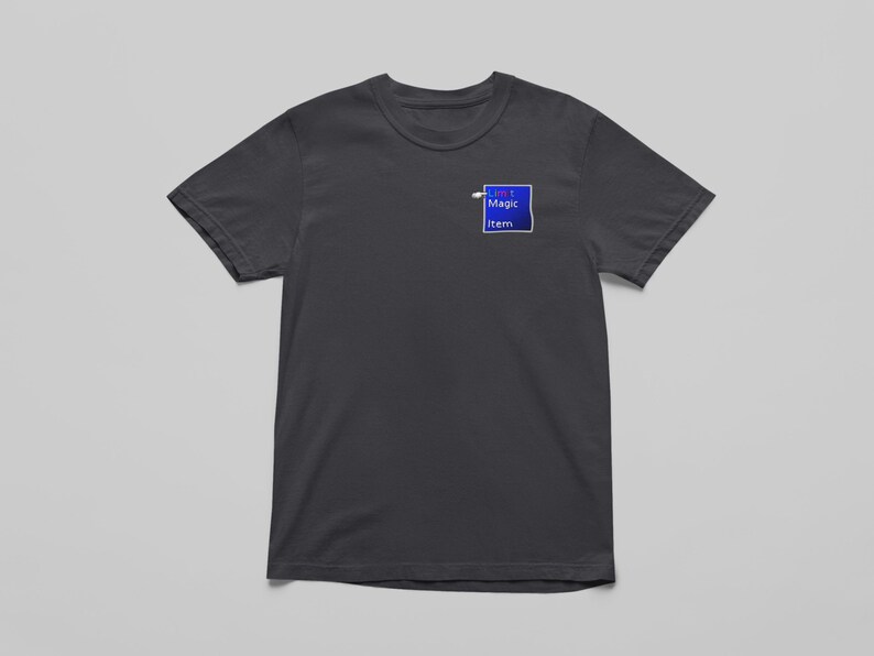 May include: Dark gray t-shirt with a crew neck. A small blue square with the text "My Magic Item" is printed on the upper left chest area. The shirt is made of a soft material and is displayed on a light gray background.