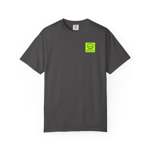 May include: Dark gray t-shirt with a neon green square graphic on the upper left chest. The graphic features a skull design and the text "SOCIETY WILL MAKE ME JAD". The shirt has short sleeves and a crew neck.