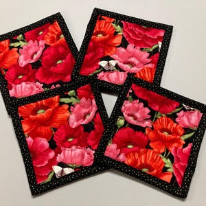 May include: Four black and white fabric coasters with a red and pink poppy flower design. The coasters have a black border with white polka dots.
