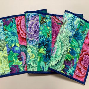 May include: A set of five colorful table runners with a floral pattern. The runners are made of fabric and have a dark blue border.