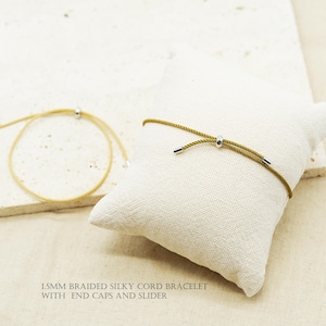 以下が含まれることがあります： 1.5mmの編み込みシルキーコードブレスレット、エンドキャップとスライダー付き。ブレスレットは2つあり、1つは明るいゴールド、もう1つは濃いオリーブグリーンです。画像には「1.5MM BRAIDED SILKY CORD BRACELET WITH END CAPS AND SLIDER」と書かれています。