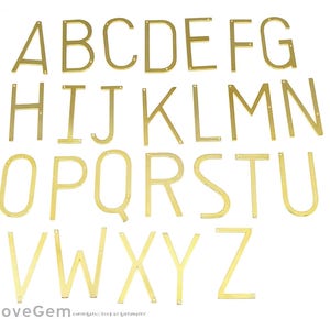 May include: Gold-colored metal alphabet letters, A through Z, in a simple, modern font style. The letters are flat and have a slightly raised edge.