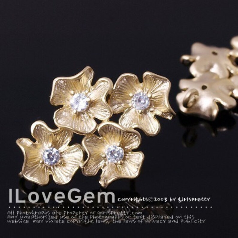 May include: A gold-toned metal connector featuring four flower-shaped components arranged in a cluster, each with a central clear round gemstone. The text ILoveGem and copyright information are visible at the bottom of the image.