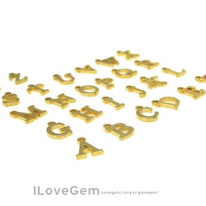 May include: Gold-colored metal alphabet letter charms. Each letter is separate and has a hole for attaching to a necklace, bracelet, or other jewelry.