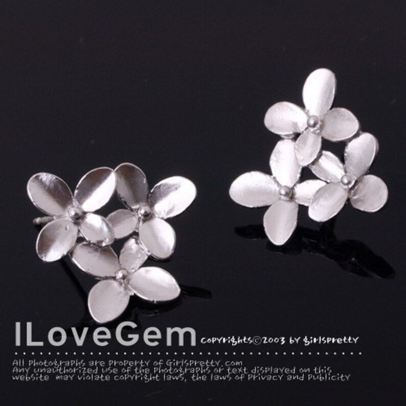 May include: A pair of silver flower-shaped earrings. Each earring features three delicate flowers clustered together.