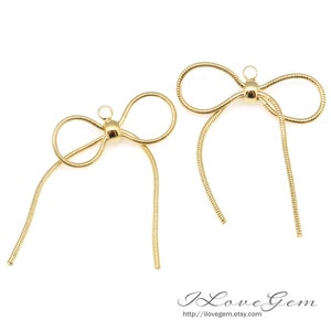 May include: Two gold-colored metal bow tie charms with long, thin chains. The bow ties are made of a snake chain design.