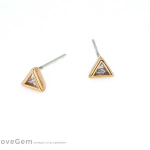 May include: A pair of gold triangle stud earrings with clear cubic zirconia stones.