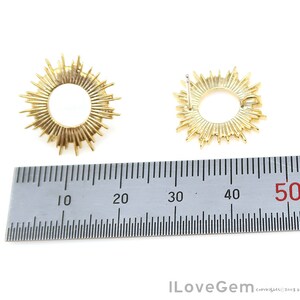 K&ouml;nnte beinhalten: Zwei goldfarbene Sonnenstrahlen-Ohrringe mit einem runden Design. Die Ohrringe werden mit einem Lineal gemessen und zeigen, dass sie einen Durchmesser von etwa 5 cm haben.