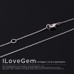 Puede incluir: Un collar de cadena de plata con un cierre de langosta y un pequeño círculo en el otro extremo. La cadena está sobre un fondo negro.