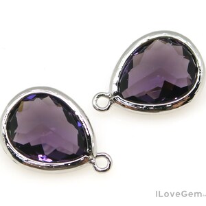 May include: Two silver teardrop-shaped pendants with clear purple glass stones.