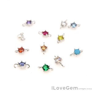 May include: Assortment of colorful gemstone charms with silver settings. The charms feature various colors, including red, blue, green, yellow, and turquoise.