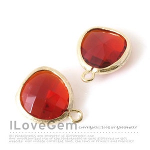May include: Two red glass heart-shaped charms with gold metal settings and a loop for hanging. The charms are on a white background.