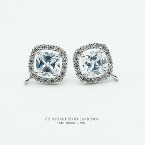 May include: Two square CZ stud earrings with a halo of smaller stones. The earrings are silver-toned and have a post backing. The text at the bottom reads "CZ SQUARE STUD EARRINGS" and "Size: approx. 10 mm."