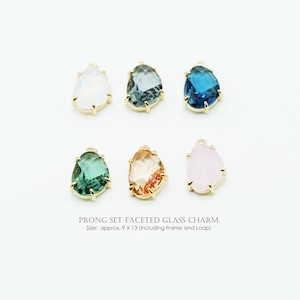May include: Six faceted glass charms in assorted colors, including white, blue, green, and pink, set in gold-coloured prongs. The charms are approximately 9 x 13 (including frame and loop). The text reads "PRONG SET FACETED GLASS CHARM".