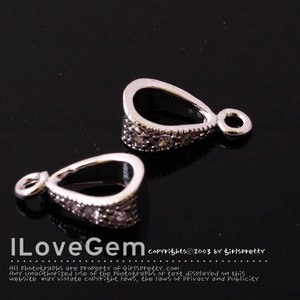 May include: Two silver-toned pendant bails with clear crystal accents. The bails are shaped like teardrops with a small loop at the top.
