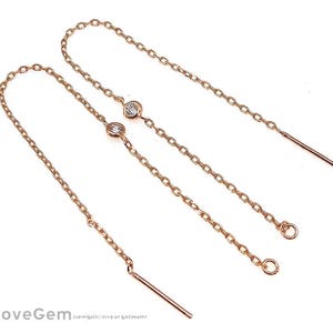 May include: A pair of rose gold dangle earrings with a small clear stone on each earring. The earrings are made of a delicate chain with a small loop at the end.