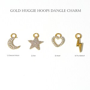 May include: Gold huggie hoop dangle charms in the shape of a crescent moon, star, heart, and lightning bolt. The crescent moon, star, and heart are encrusted with small, clear stones. The lightning bolt is solid gold.