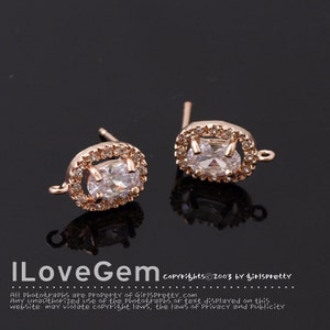 May include: A pair of gold-tone earring findings with a clear oval-shaped stone surrounded by smaller clear stones. The findings have a loop on the side for attaching a dangle.