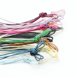May include: A collection of colorful cords with knotted ends. The cords are in various shades, including pink, purple, green, black, brown, blue, and cream. The cords are arranged on a white background.