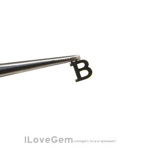 May include: A black metal letter B charm, held by tweezers.