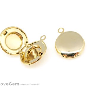 Puede incluir: Dos colgantes de medallón redondos de color dorado. Uno está abierto, revelando el interior, y el otro está cerrado. Ambos tienen un pequeño lazo en la parte superior para sujetarlos a una cadena u otro componente de joyería. Los medallones están sobre un fondo blanco.