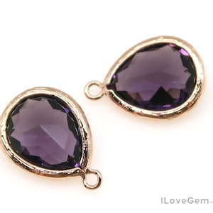 May include: Two gold-toned teardrop-shaped pendants with purple glass stones. Each pendant has a loop for attaching to a chain or cord.