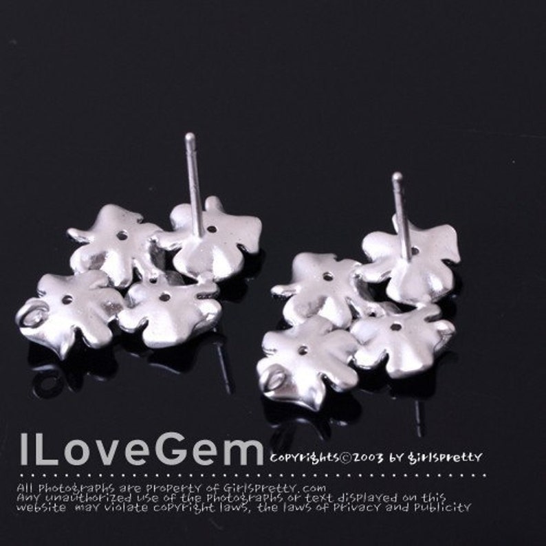 May include: A pair of silver-toned stud earrings, each featuring a cluster of four-leaf clover shapes. The earrings have a metallic finish and include a post backing. The text ILoveGem and copyright information are visible at the bottom.