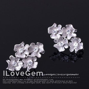 May include: A pair of silver-toned earrings, each featuring a cluster of four textured flower-shaped petals with a clear, round-cut gemstone set in the center of each bloom. The text ILoveGem and copyright information are visible at the bottom.