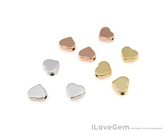 May include: Assortment of heart-shaped metal beads in gold, rose gold, and silver. The beads have a hole in the center for stringing.