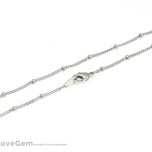 Puede incluir: Un collar de cadena de plata con cierre de mosquetón. La cadena está hecha de pequeñas cuentas redondas.