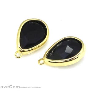 May include: Two teardrop-shaped black gemstone pendants with gold-colored bezels. Each pendant has a small loop at the top for attaching to jewelry. The gemstones have a faceted surface.