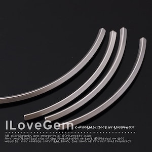 Op de afbeelding: Vier zilveren metalen hoepels, elk met een licht verschillende kromming, zijn in een waaier vorm op een zwart oppervlak gerangschikt.