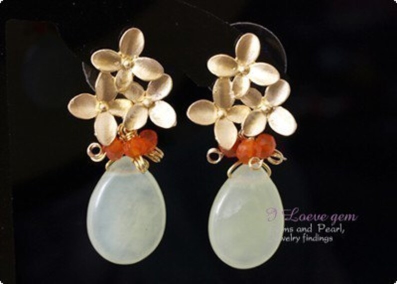 May include: A pair of dangle earrings with a light green stone drop, gold flower accents, and orange beads.