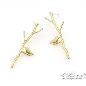 May include: A pair of gold-tone earrings featuring a delicate branch design with a small bird perched on each branch.