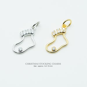 May include: Two Christmas stocking charms, one silver-toned and one gold-toned, each with a clear crystal at the toe and a crystal-studded cuff. The text reads "CHRISTMAS STOCKING CHARM" and "Size: approx. 16 X 10 mm".