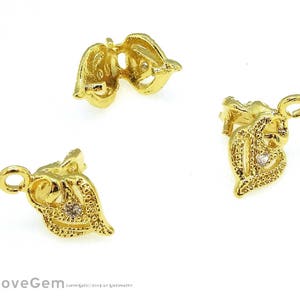 Puede incluir: Dos cierres de metal dorado con un pequeño strass transparente en el centro de cada uno. Los cierres tienen forma de corazón con detalles intrincados.