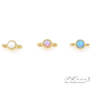 Puede incluir: Tres abalorios conectores dorados con piedras de ópalo. Los abalorios son redondos con un borde de cuentas. Los ópalos son blancos, rosados y azules.