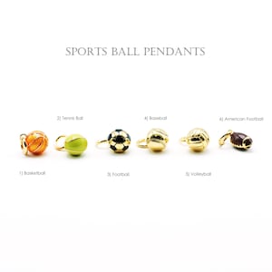 Può includere: Una collezione di ciondoli a forma di palloni sportivi, tra cui basket, tennis, calcio, baseball, pallavolo e football americano. Ogni ciondolo è dorato con disegni dettagliati, con il testo "SPORTS BALL PENDANTS" in alto.