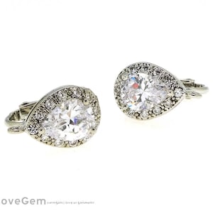 May include: A pair of silver teardrop earrings with clear cubic zirconia stones. The earrings have a halo setting and a clip-on closure.