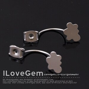May include: A pair of silver-toned earring backs with a flower-shaped design. The backs are curved and have a small hole for attaching earrings.