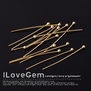 Puede incluir: Un grupo de alfileres de cabeza redonda de color dorado. Los alfileres están esparcidos sobre una superficie negra.