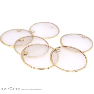 Könnte beinhalten: Sechs goldumrandete, transparente, runde Charms aus Glas oder Kunststoff mit einem Loch oben. Die Charms sind in einem Halbkreis auf weißem Hintergrund angeordnet.