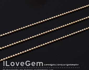 May include: Three strands of gold ball chain, a type of jewelry chain, are displayed on a black surface. The chain is made of small, round beads.