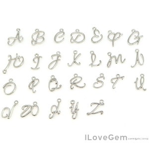 Könnte beinhalten: Silberne Metall-Anhänger in Form von Buchstaben in Schreibschrift. Die Anhänger sind in alphabetischer Reihenfolge von A bis Z angeordnet.