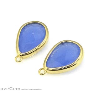 Peut inclure: Deux pendentifs en forme de goutte d'eau avec des pierres précieuses bleues et des bordures dorées. Chaque pendentif a une surface facettée et une petite boucle en haut pour l'attache. Les pierres sont bleu clair.