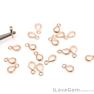 Puede incluir: Una colección de 18 hallazgos de joyería de metal dorado, cada uno con forma de lágrima con un bucle en la parte superior. Estos hallazgos son ideales para agregar un toque de elegancia a los proyectos de joyería.