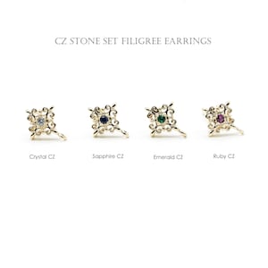 Op de afbeelding: Goudkleurige filigraan oorbellen met CZ-stenen in kristal, saffier, smaragd en robijn. De oorbellen hebben een vierkant ontwerp met een centrale steen en decoratieve krullen. De tekst luidt "CZ STONE SET FILIGREE EARRINGS".