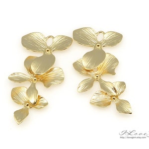 May include: A pair of gold-tone metal flower charms with a textured finish. Each charm features three layered flowers with a loop at the top for attaching to jewelry.